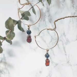 May include: A pair of gold hoop earrings with a dangling red and black gemstone charm.