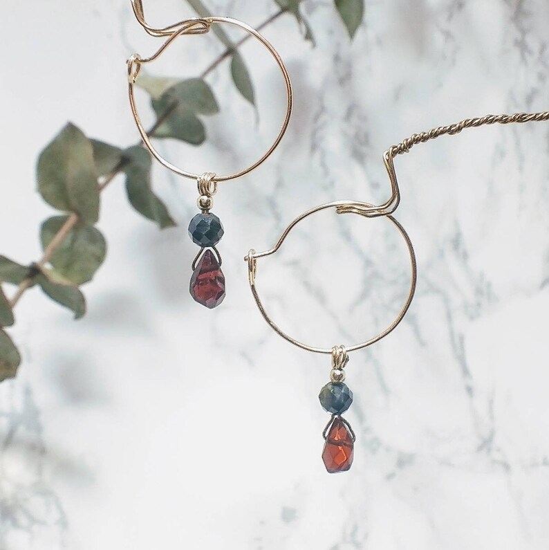 May include: A pair of gold hoop earrings with a dangling red and black gemstone charm.
