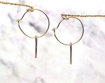 May include: A pair of gold hoop earrings with a small, straight, dangling piece attached to each hoop.