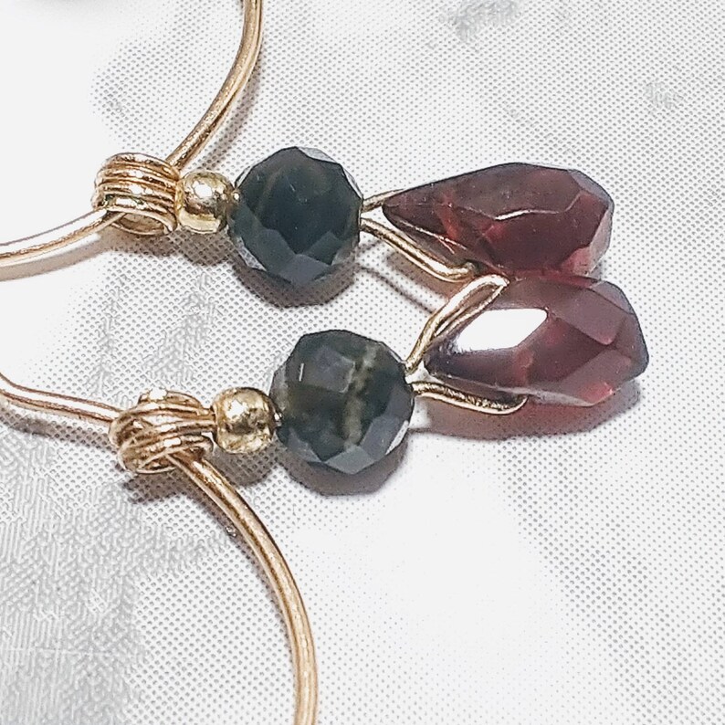 May include: Gold hoop earrings with a black and green gemstone and two red teardrop-shaped gemstones.