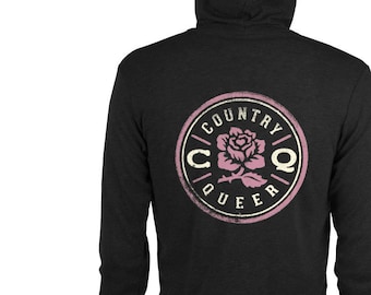 Puede incluir: Una sudadera con capucha negra con un logotipo circular desgastado que presenta una rosa rosa y el texto "COUNTRY QUEER".