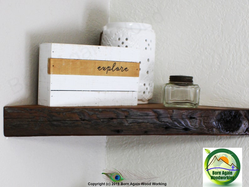 Op de afbeelding: Een rustiek houten hoekplank met een witte doos waarop "explore" staat. Er staat een glazen pot en een wit decoratief object op de plank.