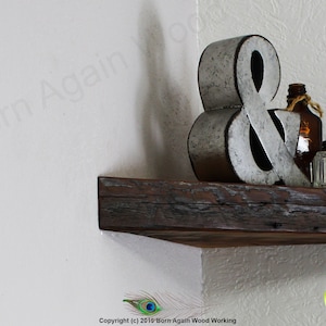 Op de afbeelding: Een rustiek houten hoekplank met een metalen ampersand, een glazen fles en een glazen pot erop. De plank is gemaakt van gerecycled hout en heeft een natuurlijke afwerking.