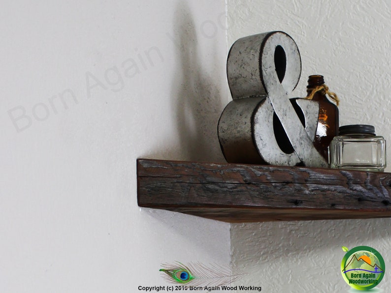Op de afbeelding: Een rustiek houten hoekplank met een metalen ampersand, een glazen fles en een glazen pot erop. De plank is gemaakt van gerecycled hout en heeft een natuurlijke afwerking.