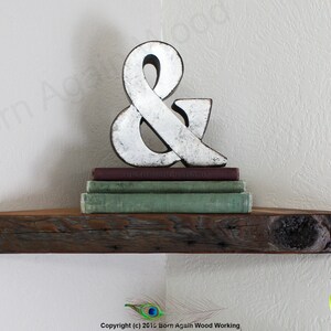 Op de afbeelding: Een rustiek houten hoekplank met een verweerde afwerking. De plank is versierd met een zilveren ampersand en een stapel boeken.