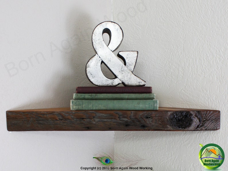 Op de afbeelding: Een rustiek houten hoekplank met een verweerde afwerking. De plank is versierd met een zilveren ampersand en een stapel boeken.