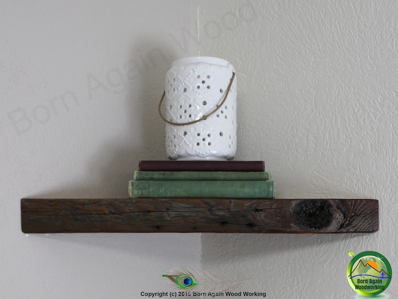 Op de afbeelding: Een rustiek houten plank met een witte decoratieve kaarsenhouder en een stapel boeken erop. De plank is gemonteerd aan een lichtbeige muur.