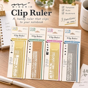 May include: Four Midori Clip Rulers in gold, copper, and silver tones, each on individual white backing cards. These metal tools feature cut-out templates, a straight edge, and a clip function. The packaging displays the text Clip Ruler, 3 functions in one, and 0.3mm thickness, showcasing various icon designs.