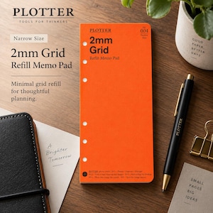 May include: A bright orange Plotter 2mm Grid Refill Memo Pad in narrow size with five punched holes along the left edge. The cover features black text including the brand name, grid specifications, and the number 004. A black pen rests nearby.