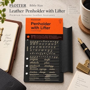 May include: A black leather penholder with lifter for Bible size planners, featuring an orange header card with the text Penholder with Lifter Cursive Sample. The black insert displays gold cursive alphabet letters and practice words.