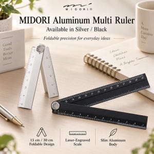 Op de afbeelding: Een Midori aluminium multi-liniaal in zilver en zwart. De zilveren liniaal is in een driehoek gevouwen, terwijl de zwarte liniaal is uitgeklapt tot een lengte van 30 cm. Beide hebben lasergegraveerde schaalverdelingen en een scharnier.