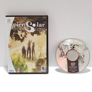 Puede incluir: Una caja y un disco de videojuego de Dreamcast para "Pier Solar and the Architects". La caja negra tiene una cubierta colorida con siluetas. El disco tiene una superficie plateada con arte de personajes.