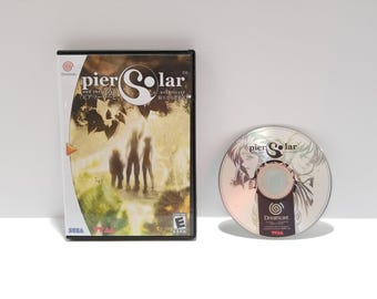 May include: A Dreamcast video game case and disc for "Pier Solar and the Architects". The case is black with a colorful cover featuring silhouetted figures. The disc has a silver surface with character art.