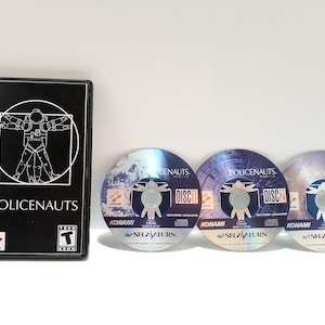 May include: A SEGA Saturn game, "POLICENAUTS", with a black case featuring a white illustration of a spaceman. Three game discs are displayed, labeled "DISC 1", "DISC 2", and "DISC 3". The discs have a blue and white design.