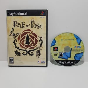 Puede incluir: Caja y disco de videojuego de PlayStation 2 para "Rule of Rose". La caja presenta un fondo beige con un diseño de rosa, una mariposa y un conejo. El disco tiene un diseño de mariposa azul y el título del juego.