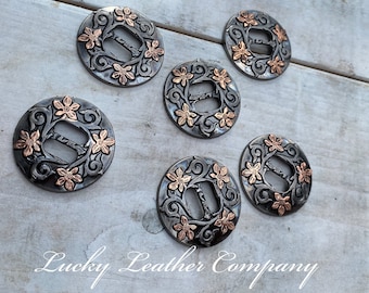 May include: Six silver and copper conchos with floral designs. The conchos have a cutout in the center and are perfect for adding a touch of western style to your leather goods.