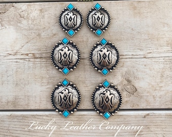 May include: Six silver-toned metal conchos with turquoise accents and an eagle design. The conchos are arranged in two rows of three on a wooden surface.  "Lucky Leather Company" is written in black text at the bottom of the image.