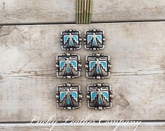 May include: Six silver-toned metal conchos with turquoise blue inlay and a geometric design. The conchos are arranged in two rows of three.  The conchos are on a light wood background.  Lucky Leather Company is written in black text at the bottom of the image.