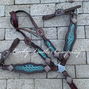 May include: A turquoise and brown leather horse bridle with silver and copper accents. The bridle is laid out on a brick surface. The text "Lucky Leather Company" is visible in the image.