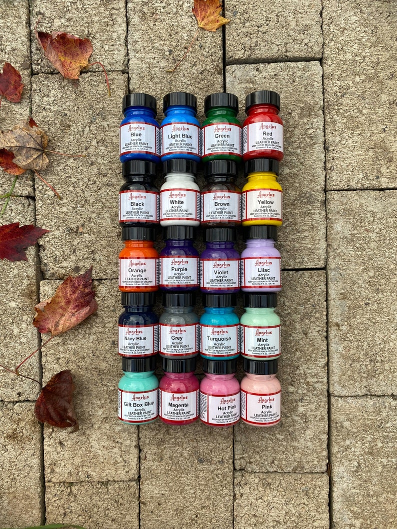 Puede incluir: Una colecci&oacute;n de 18 peque&ntilde;os frascos de pintura acr&iacute;lica para cuero Angelus en varios colores, incluyendo azul, verde, rojo, negro, blanco, marr&oacute;n, amarillo, naranja, morado, violeta, lila, azul marino, gris, turquesa, menta, azul caja de regalo, magenta, rosa intenso y rosa. Los frascos est&aacute;n dispuestos en cuatro filas de cuatro frascos cada una, y todos est&aacute;n sobre una superficie de piedra.