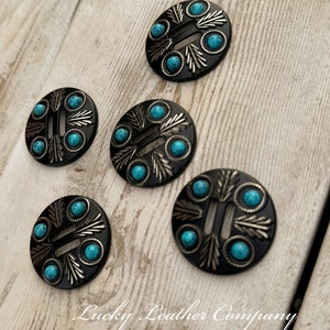May include: Five turquoise and silver concho buttons with a decorative design. The buttons are round and have a black background. The buttons are arranged in a semi-circle on a light wood surface.  Lucky Leather Company is written in black text on the surface.