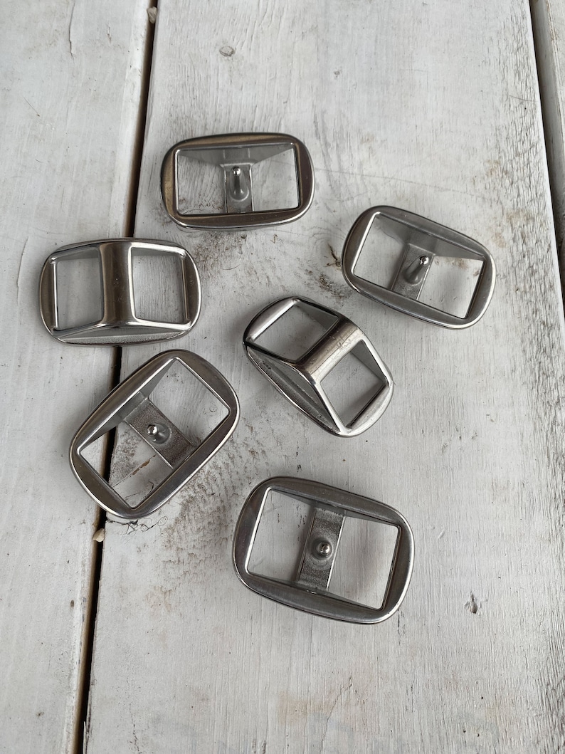 May include: Six silver metal belt buckles with a rectangular shape and a small hole in the center.