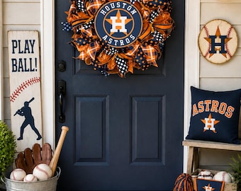 Könnte beinhalten: Ein Houston Astros Dekorationsset für den Eingangsbereich mit einem Kranz aus Netzstoff mit orangefarbenen und marineblauen Punkten, einem Holzschild mit der Aufschrift PLAY BALL, einem marineblauen Kissen mit Astros-Logo und einer Fußmatte mit HOME SWEET HOME.
