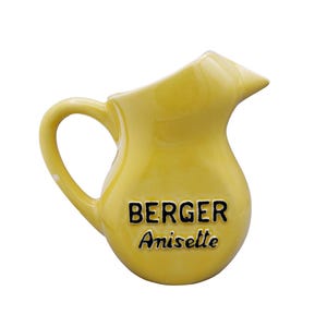 Peut inclure: Petite cruche en céramique jaune avec une anse et un bec verseur. L'inscription "BERGER Anisette" est imprimée en noir sur le devant. La cruche est isolée sur fond blanc.
