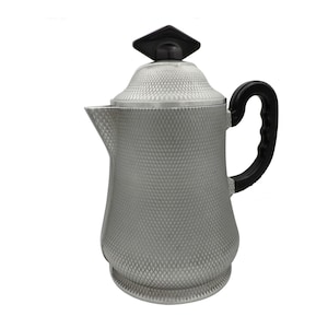 Peut inclure: Cafetière argentée avec un motif en losanges texturé. Elle possède une poignée noire et un bouton de couvercle noir de forme carrée. Le bec verseur est incliné.