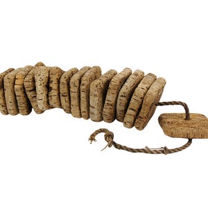 Op de afbeelding: Een natuurlijk badspeelgoed van kurk, bestaande uit een reeks verbonden, afgeronde kurkstukken. Een vierkant kurkstuk is bevestigd met een gedraaid touw. Het speelgoed is gemaakt van lichtbruin kurkmateriaal.