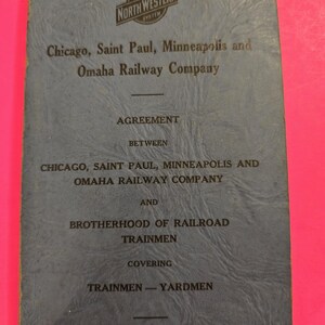 May include: A vintage blue booklet with the Chicago and North Western System logo. The cover reads "Chicago, Saint Paul, Minneapolis and Omaha Railway Company" and "Agreement Between... Brotherhood of Railroad Trainmen." The effective date is October 1, 1946.