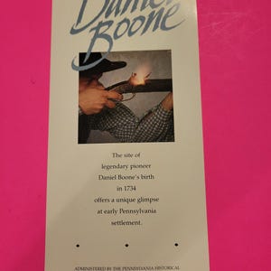 May include: A brochure with the title "Daniel Boone" in a stylized script. The brochure features an image of a person firing a rifle and text describing Daniel Boone's birth in 1734 and the early Pennsylvania settlement.