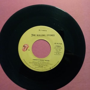 May include: A black vinyl record with a yellow label. The label features the text "RS 7-99978", "THE ROLLING STONES", "TWENTY FLIGHT ROCK", "PRODUCED BY THE GUNNER THING", "Recorded by Bob Clearmountain and David Hewitt", "Mixed by Bob Clearmountain", "From Rolling Stones "STILL LIFE" COC 30113", "45 R.P.M.", "STEREO", "Published by ABKCO Music Inc. (BMI)", "Music: Mick Jagger", "Words: Mick Jagger", "Time: 3:42", "VOCAL", "57-45-43205-SP", "℗ 1982", "Promotion B.V."