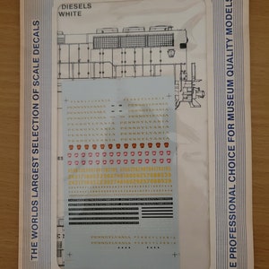 May include: A Microscale Decal sheet for model railway enthusiasts. The sheet features decals for Pennsylvania Railroad diesel locomotives. The decals are in red, white, and gold. The sheet is labelled "The World's Largest Selection of Scale Decals" and "The Professional Choice for Museum Quality Models".