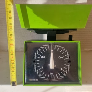 May include: A green kitchen scale with a black face and a white needle. The scale has a dial that reads from 0 to 3 grams and has markings for 0.5, 1, 1.5, 2, 2.5, and 3 grams. The scale is made by EKS.