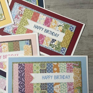 May include: Handmade birthday cards with colorful patterned paper designs. Each card features a rectangular patchwork design with a white banner that reads "HAPPY BIRTHDAY". The cards are on a light wood grain surface.