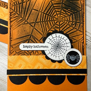 May include: Orange card with a black spider web pattern, a black spider web with a white center, a black spider with white eyes, and the text "happy halloween".
