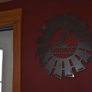 May include: A black metal wall decor in the shape of a windmill with a circle in the center that says "Lucas" with a stylized "L" in the circle.