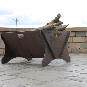 May include: A large, rectangular metal fire pit with a rustic brown finish. The fire pit has a wide opening and a raised lip around the edge. It is sitting on a concrete patio.
