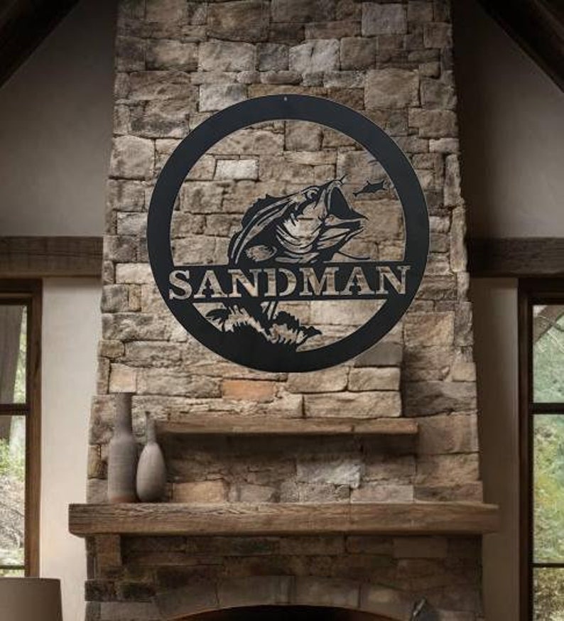 May include: Black metal wall art featuring a fish leaping out of the water, set within a circular frame. The word "SANDMAN" is displayed below the fish. The artwork is mounted on a stone wall above a fireplace, creating a rustic aesthetic.