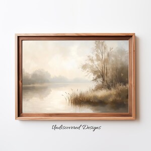 Puede incluir: Una pintura enmarcada que representa una escena de lago brumoso con un solo árbol en el lado derecho de la imagen. El lago está tranquilo y reflectante, y el cielo es de un azul suave y apagado. La pintura está en un marco de madera.