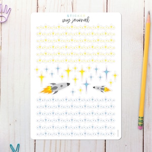 May include: A sheet of stickers with a space theme. The stickers feature blue and yellow stars, rockets, and lines of stars. The sheet is labeled "Sticker my journal".