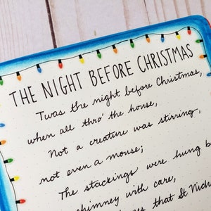 Puede incluir: Una p&aacute;gina con el texto THE NIGHT BEFORE CHRISTMAS seguido de las primeras l&iacute;neas del poema en tinta negra. El borde est&aacute; decorado con una guirnalda de luces navide&ntilde;as dibujada a mano en rojo, naranja, verde y azul sobre fondo blanco.