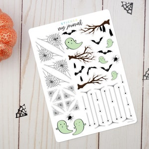 May include: A white sticker sheet labeled Sticker my journal featuring Halloween-themed designs including black spiderwebs, brown bare tree branches, small black bats, a black spider, and several light green cartoon ghosts with simple faces.