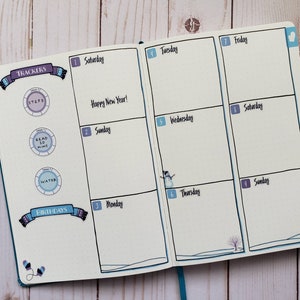 May include: A weekly planner with a winter theme. The planner has a blue cover and is open to the week of January 1st. The days of the week are labeled with numbers and the days of the week. The planner has a section for trackers and birthdays. The trackers include steps, read 30 mins, and water. The planner has a wintery design with snowflakes and a snowman.