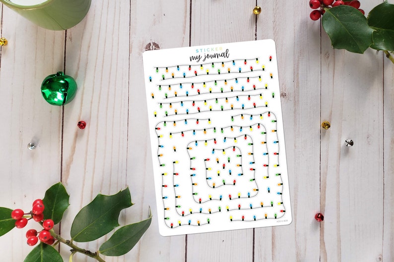 Puede incluir: Una hoja de pegatinas rectangular blanca con el texto "STICKER my journal" en la parte superior. La hoja presenta un patr&oacute;n de cables negros con peque&ntilde;as bombillas navide&ntilde;as de colores rojo, amarillo, azul y verde dispuestas en filas y cuadrados.