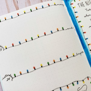 Puede incluir: Una p&aacute;gina de diario con l&iacute;neas negras dibujadas a mano y bombillas navide&ntilde;as de colores. El texto incluye Thursday 22, Friday 23, Saturday 24 y el poema The Night Before Christmas escrito en tinta negra con un borde de acuarela azul.