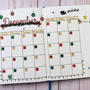May include: A December calendar planner with a festive Christmas theme. The calendar features a wreath with lights, ornaments, and gift boxes. The days of the week are labeled, and there are spaces for writing notes.