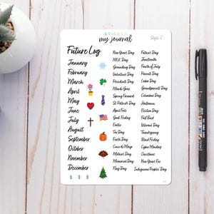 May include: A white sticker sheet with the text "Future Log" and a list of months and holidays. The sticker sheet is next to a black pen, a blue notebook, and a small succulent in a white pot.