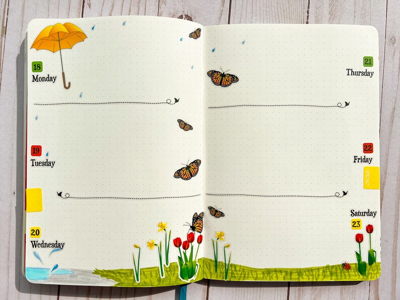 May include: A weekly planner with a yellow umbrella, butterflies, and flowers. The days of the week are labeled Monday through Saturday. The numbers 18 through 23 are written on the page.